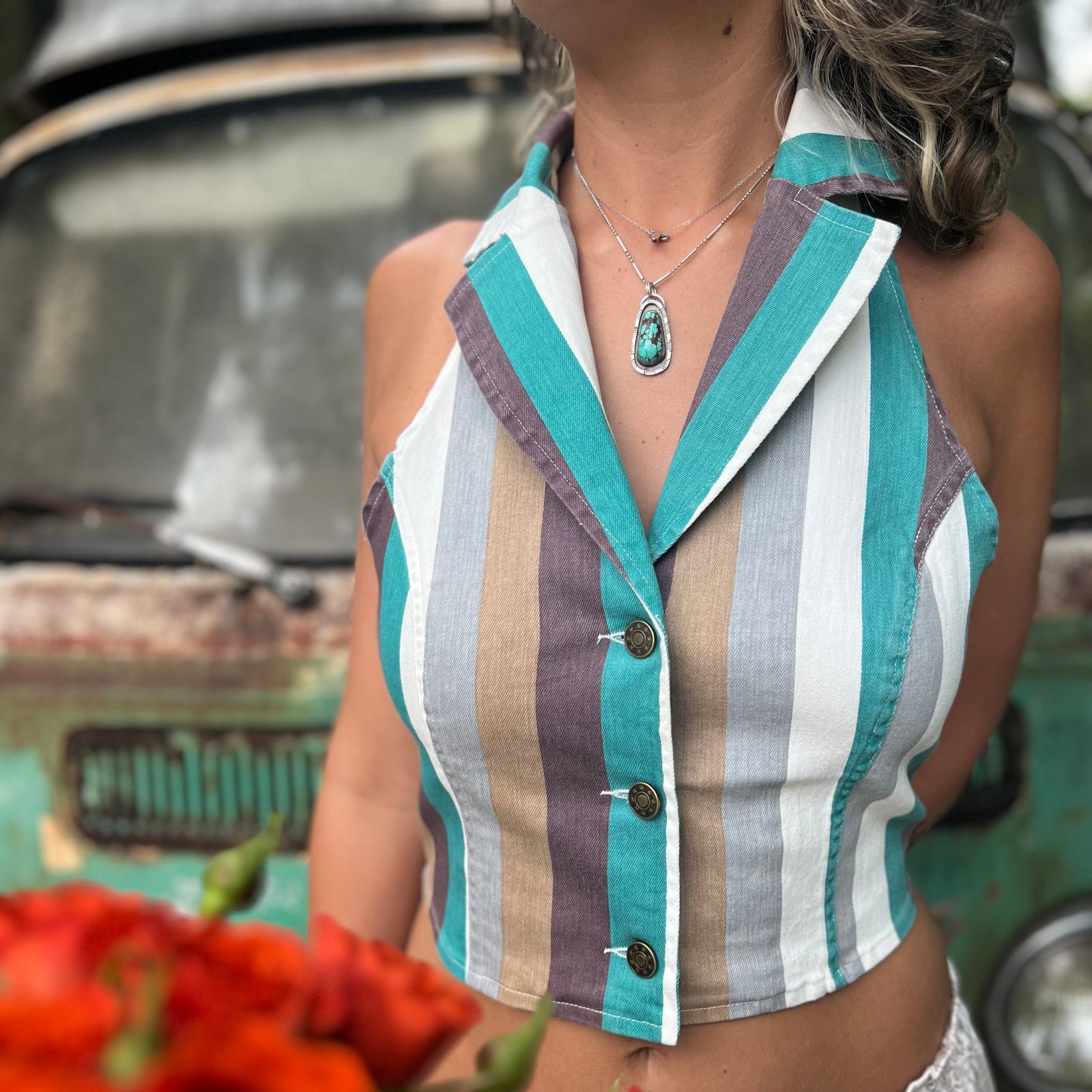 Someone wearing the turquoise multi Retro Striped Denim Halter Vest Top while holding red flowers.