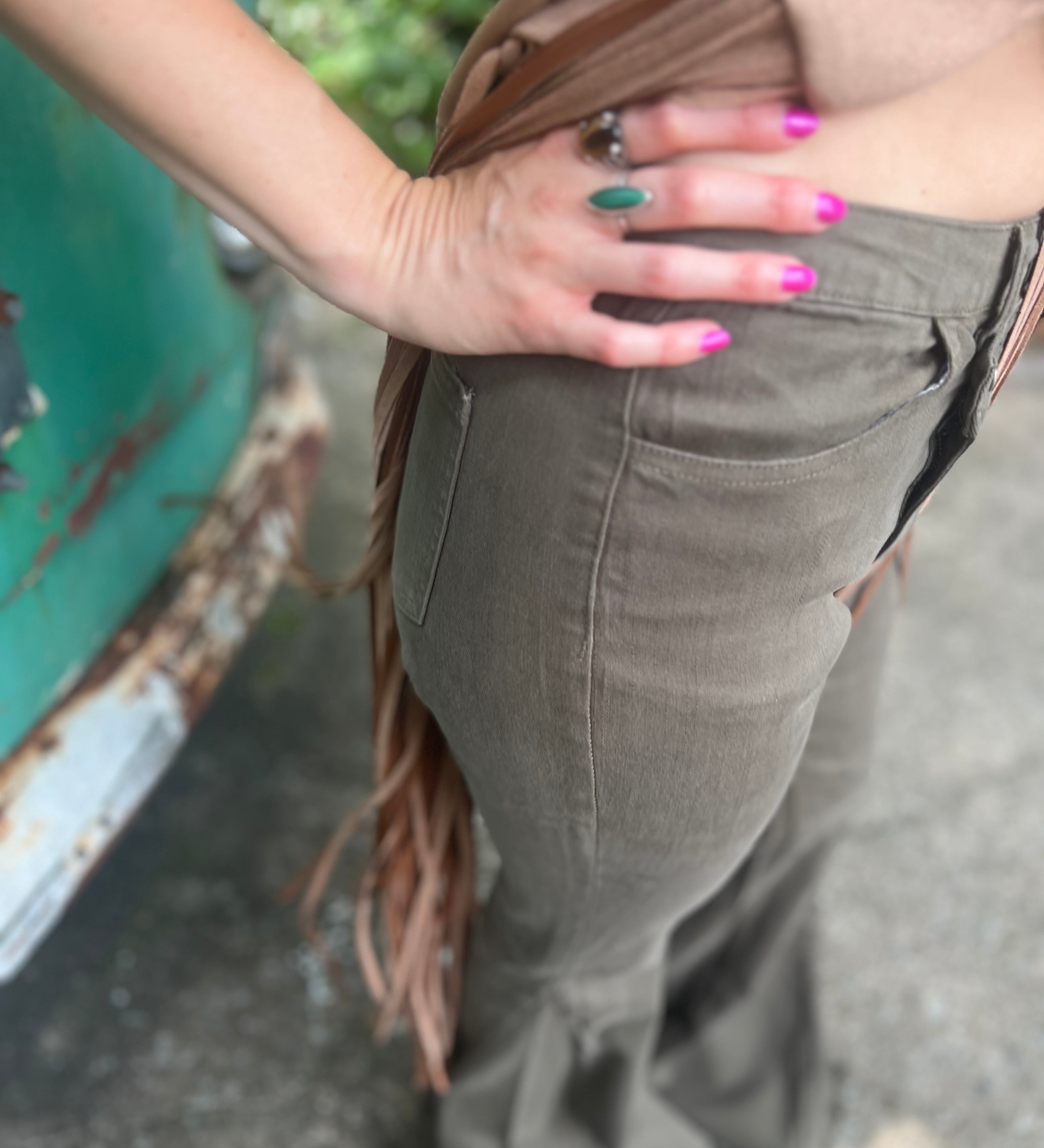 Someone wearing the Olive Criss Cross Upsized Bell Bottom Jean with a fringe vest.