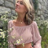 Stylish woman looking upward while standing in front of wildflowers, wearing a crochet crop top and long earrings