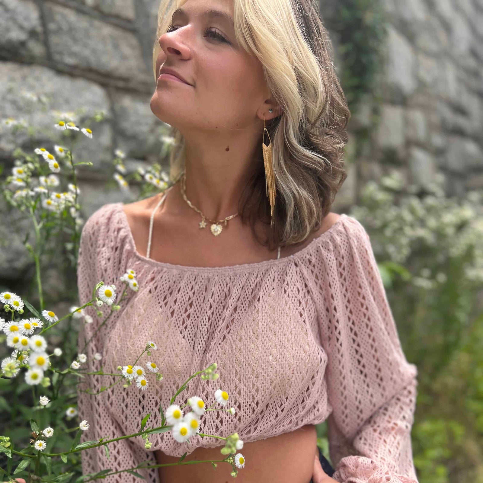Stylish woman looking upward while standing in front of wildflowers, wearing a crochet crop top and long earrings