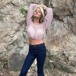Full-body shot of woman in embroidered bell-bottom jeans and boho knit crop top, standing with arms stretched above her head