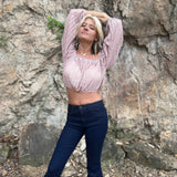 Full-body shot of woman in embroidered bell-bottom jeans and boho knit crop top, standing with arms stretched above her head