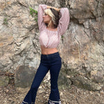 Stylish woman striking a pose with arms behind her head, wearing flare jeans with embroidered patterns and a pink crochet blouse