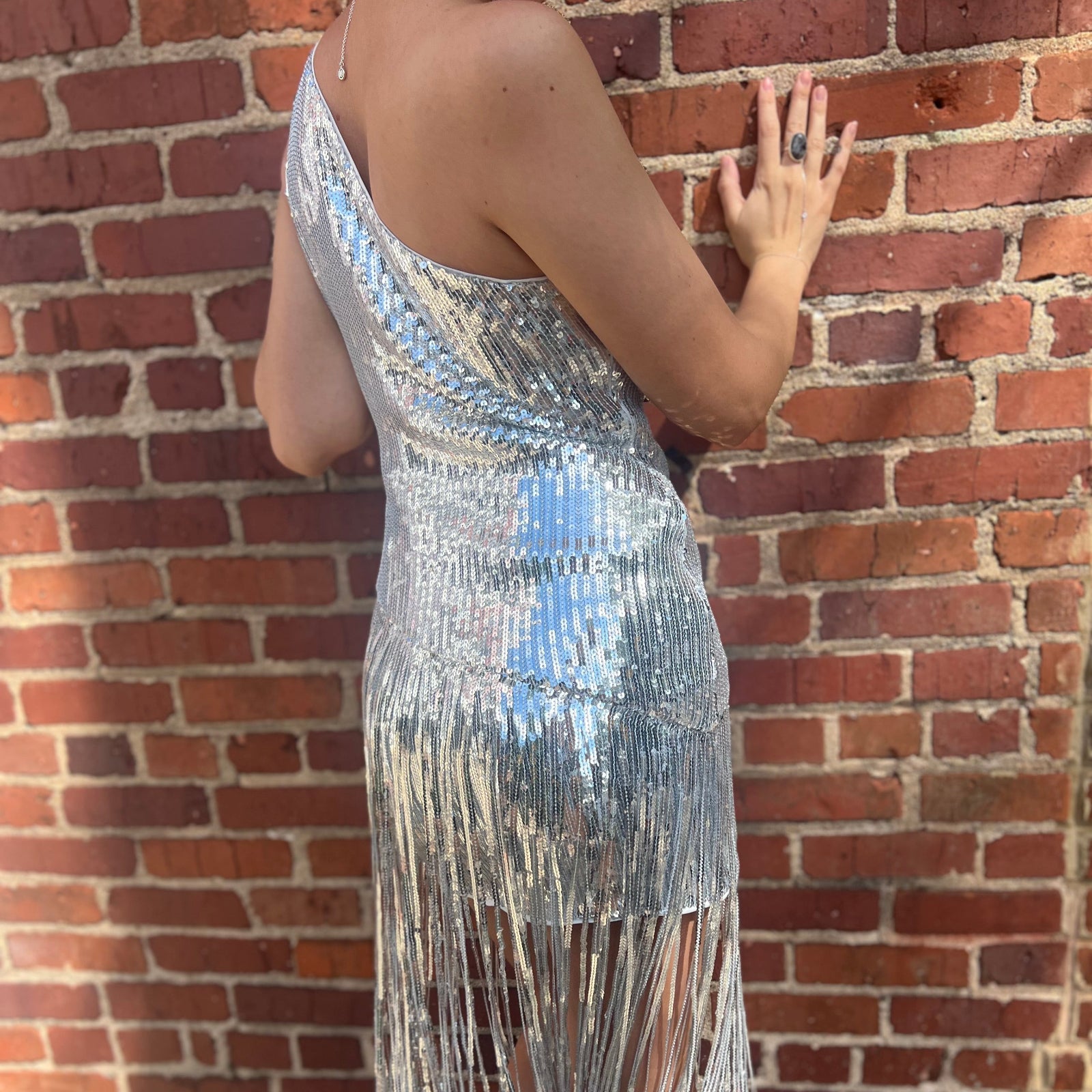 A woman wearing the Silver Sequin Disco Dress in front of a brick building.