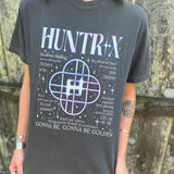 A woman wearing the Huntrix Kpop Demon Hunters Inspired Cotton Tee with jeans in front of a wooden fence.
