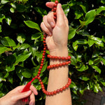 model holding red jasper mala weaved in her hands on a greenery background