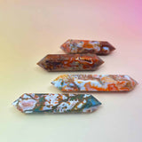 Four polished red moss agate double-terminated points in varying red, green, and white tones on a peach-pink background