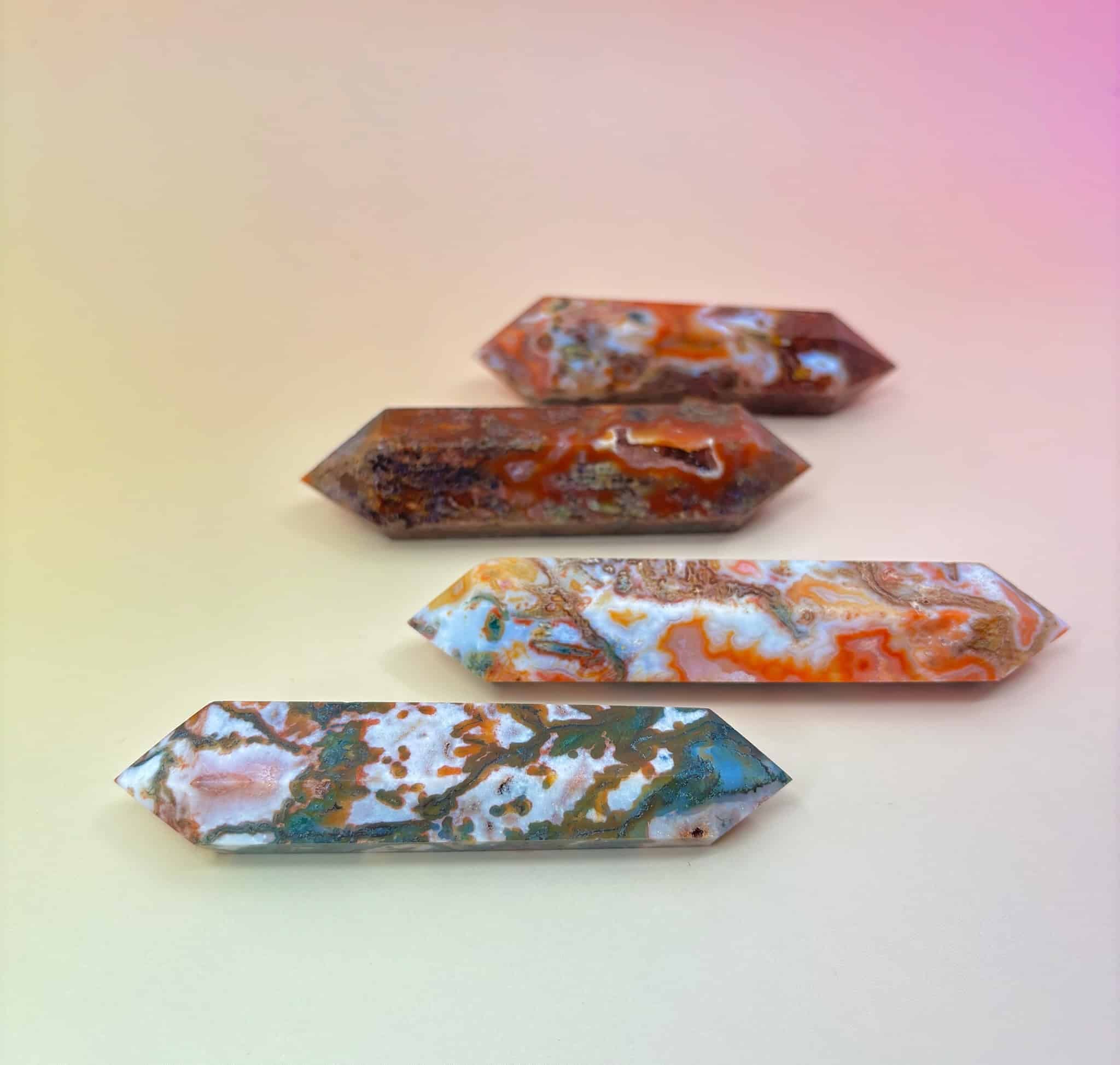Four polished red moss agate double-terminated points in varying red, green, and white tones on a peach-pink background