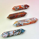 Four polished red moss agate double-terminated points in varying red, green, and white tones on a peach-pink background
