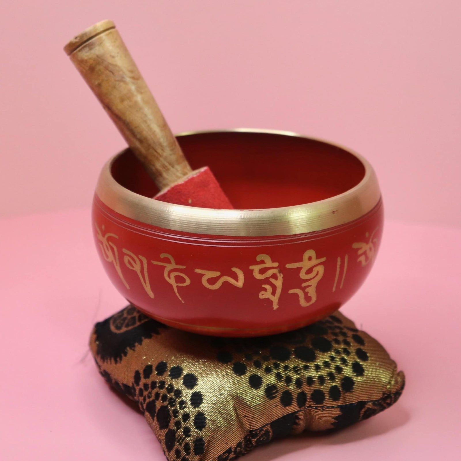 Red singing bowl with gold rim and text on a decorative pillow against a pink background