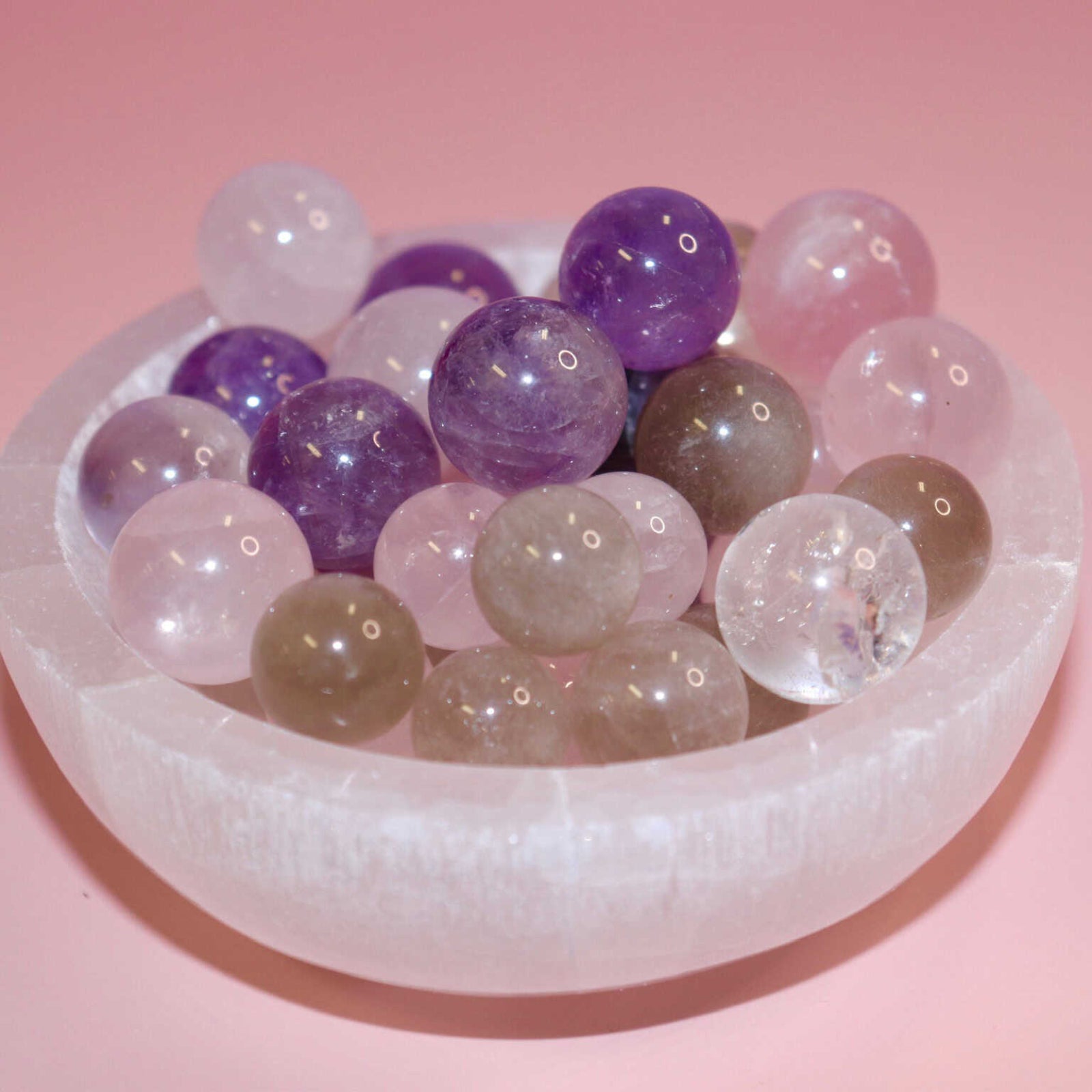 selenite bowl full of small crystal marbles on a pink background