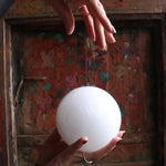 Hand holding a white sphere in front of a decorative wooden background