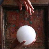 Hand holding a white sphere in front of a decorative wooden background