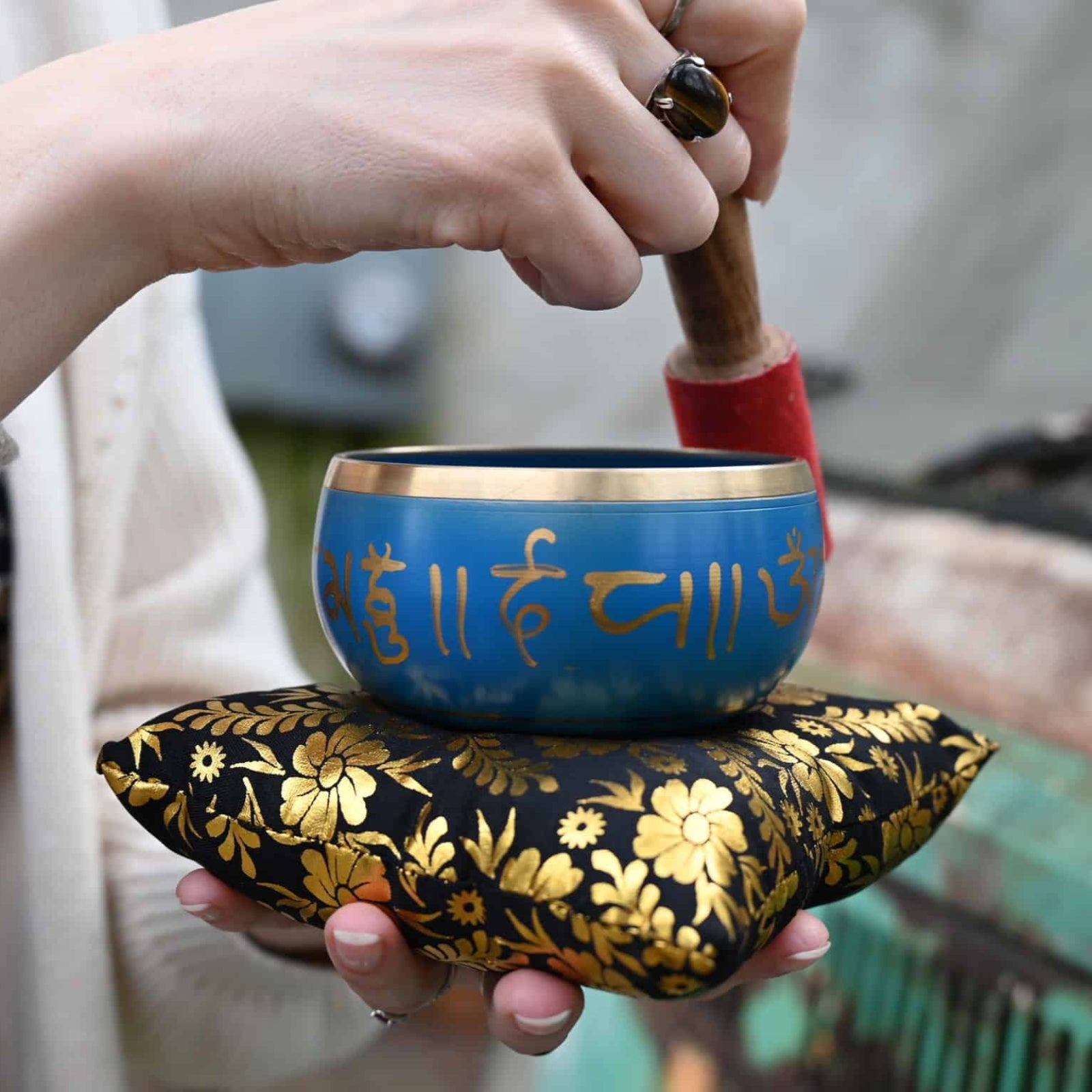 Person holding a blue singing bowl with floral design on a blurred background
