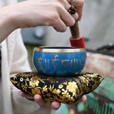 Person holding a blue singing bowl with floral design on a blurred background