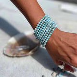 Larimar beaded bracelet on a wrist with a shell and stones in the background