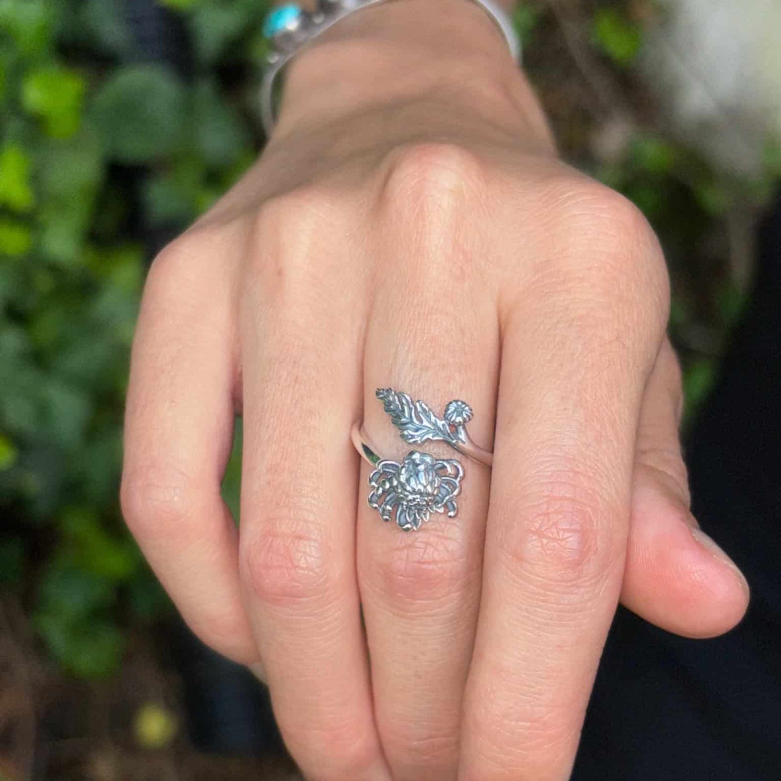 Hand wearing a silver ring with a decorative design against a blurred green background