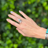 Hand wearing a ring with turquoise stones against a green leafy background