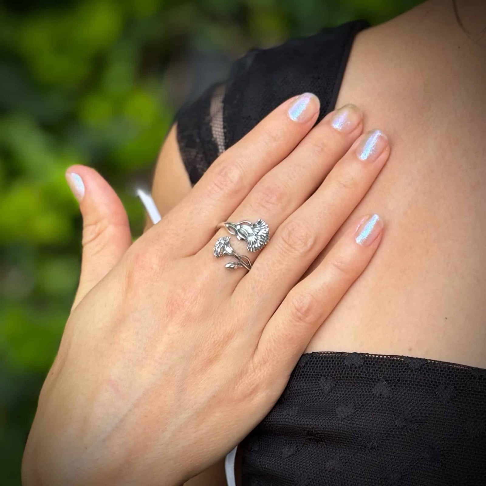 Hand with a silver ring on a blurred green background