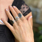 Close-up of a hand wearing multiple rings with a blurred natural background