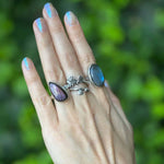 Hand wearing multiple rings with purple gemstones against a green blurred background