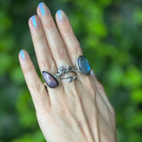 Hand wearing multiple rings with purple gemstones against a green blurred background