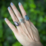 Hand wearing multiple silver rings with gemstones against a blurred green background