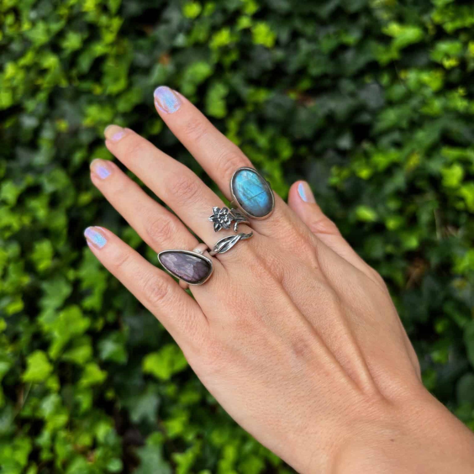 Hand wearing multiple rings with a green leafy background