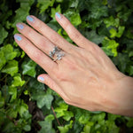 Hand wearing a silver ring with a green leafy background
