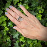 Hand wearing a silver ring with a green leafy background