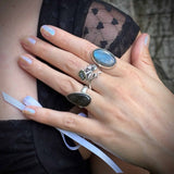 Close-up of a hand wearing multiple silver rings with gemstones, against a blurred background.