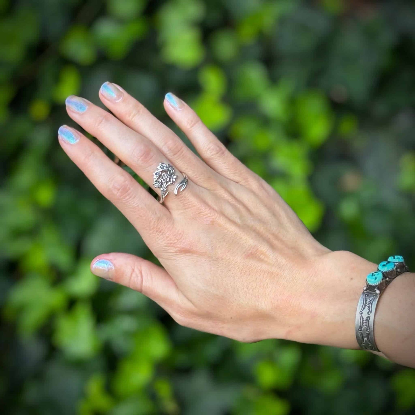 Hand wearing a silver ring with a green leafy background