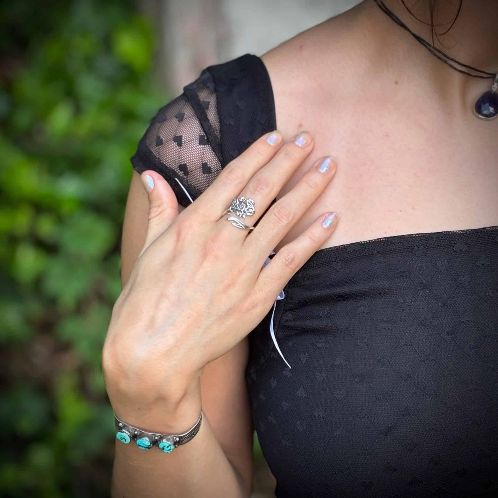 Person wearing a black dress with sheer sleeves, holding hand to shoulder, against a blurred green background
