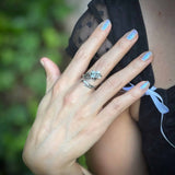 Hand with a silver ring and blue nail polish holding a black lace garment against a blurred green background