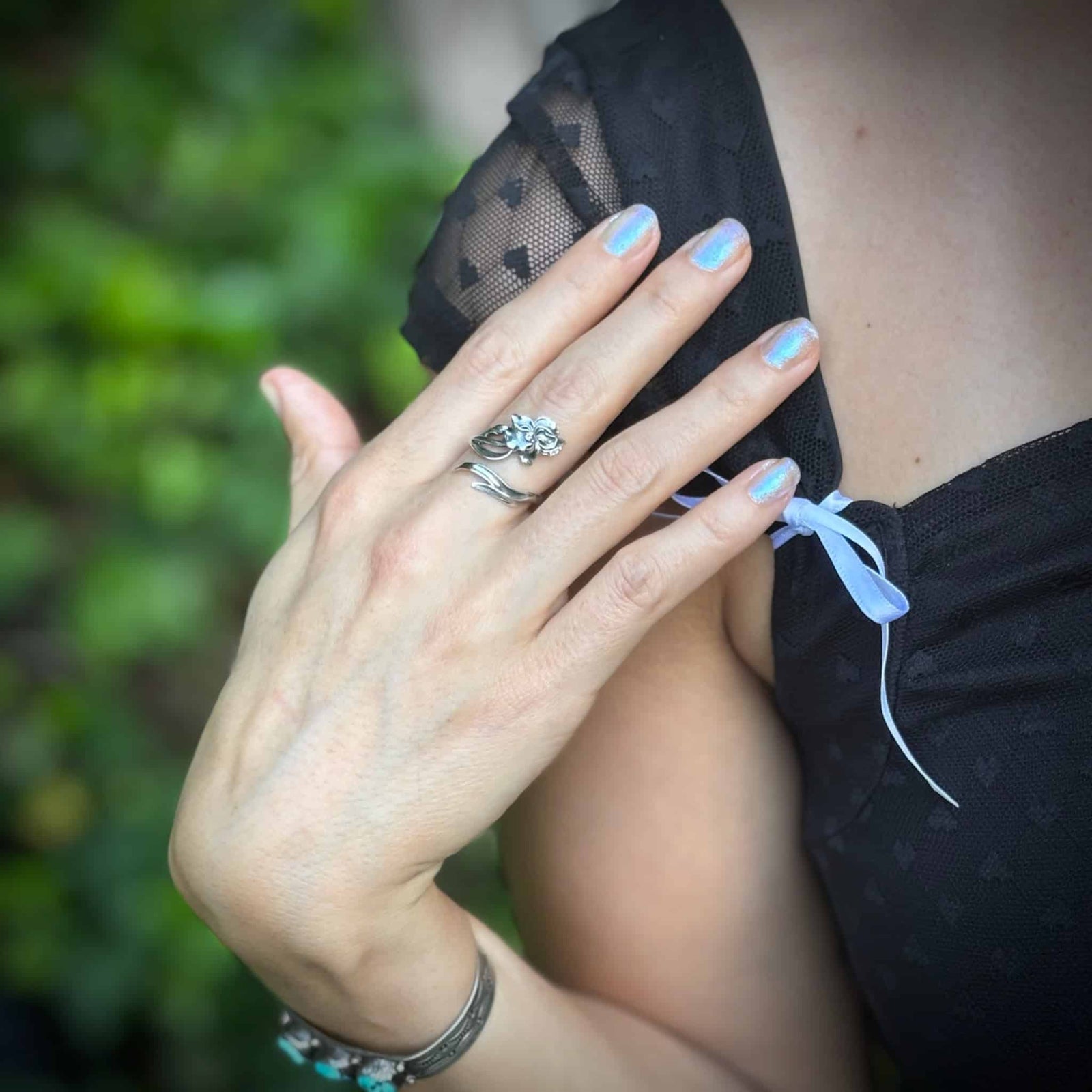 Person wearing a black top with sheer panels and a ring, against a blurred green background