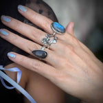 Close-up of a hand wearing two silver rings with blue stones on a blurred background