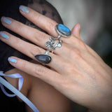 Close-up of a hand wearing two silver rings with blue stones on a blurred background