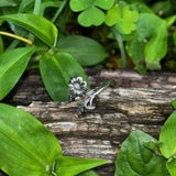 Silver ring with floral design on a wooden log surrounded by green leaves
