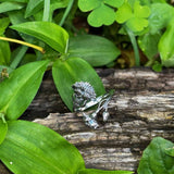 Silver ring with a black and white pattern on a wooden log surrounded by green leaves