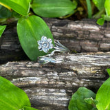 Silver flower-shaped ring on a wooden surface with green leaves
