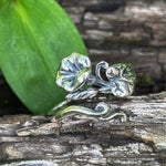 Silver ring with leaf design on a wooden surface with green leaves