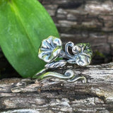 Silver ring with leaf design on a wooden surface with green leaves