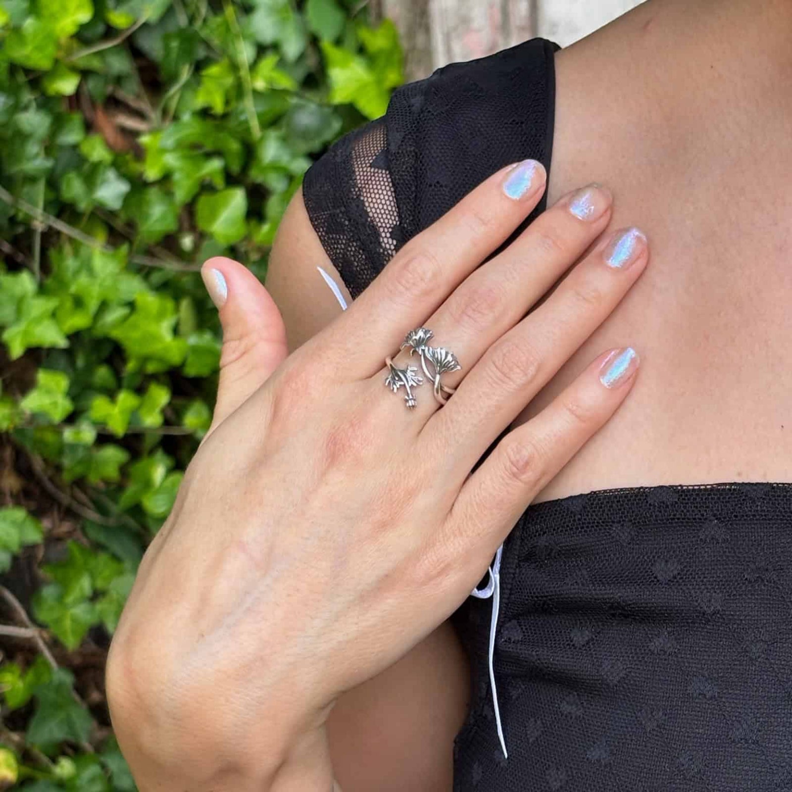 Person wearing a black top with lace detailing, turquoise bracelet, and silver ring against a green leafy background.