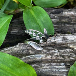Silver ring with a leaf design on a wooden log surrounded by green leaves