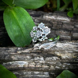 Silver floral ring on a wooden surface with green leaves