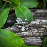 Silver floral earring on a wooden log with green leaves