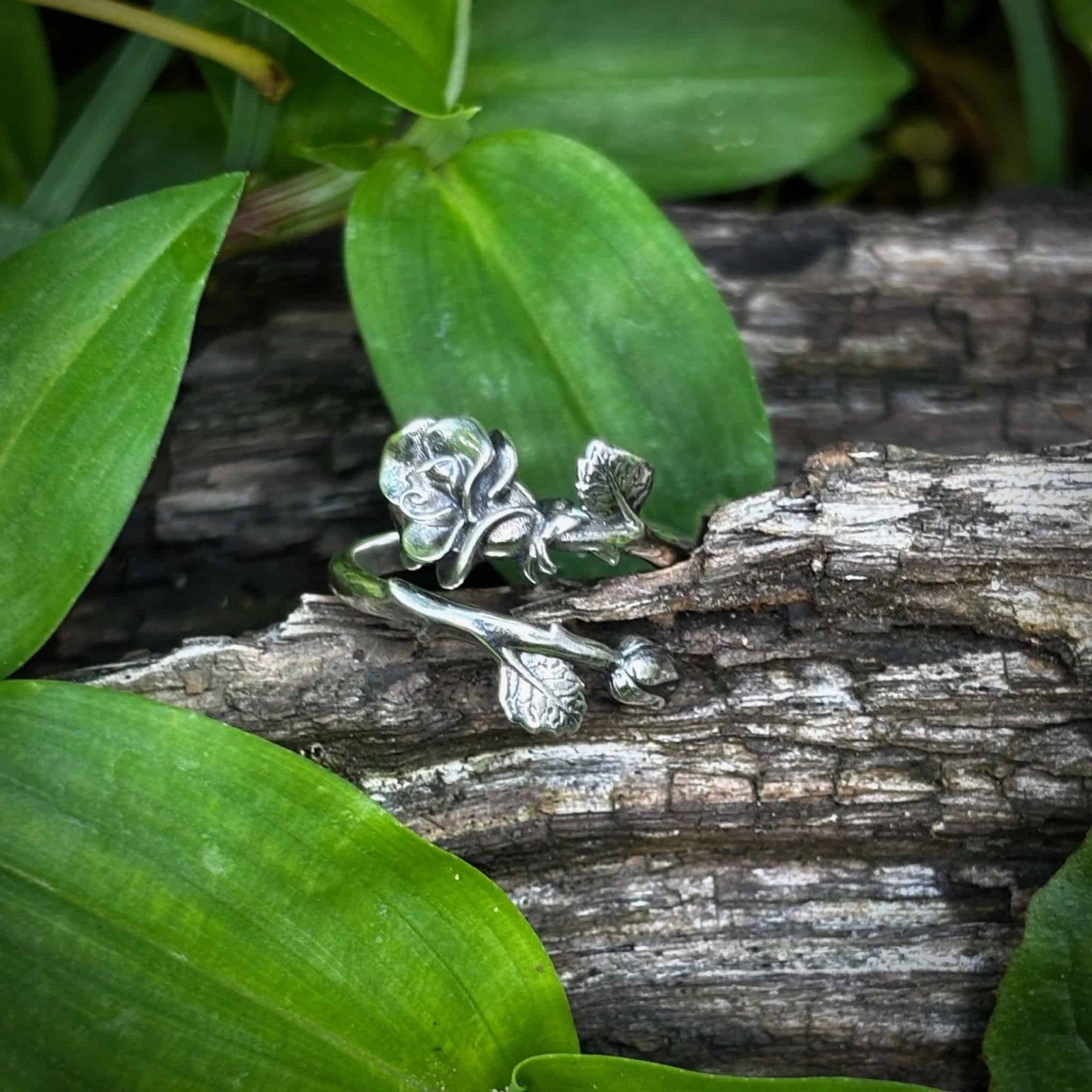 Silver floral earring on a wooden log with green leaves