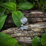Silver leaf-shaped object on a wooden log with green leaves in the background