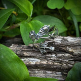 Silver leaf-shaped ring on a wooden log with green leaves in the background