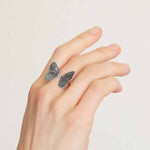 Silver butterfly ring on a hand against a plain background
